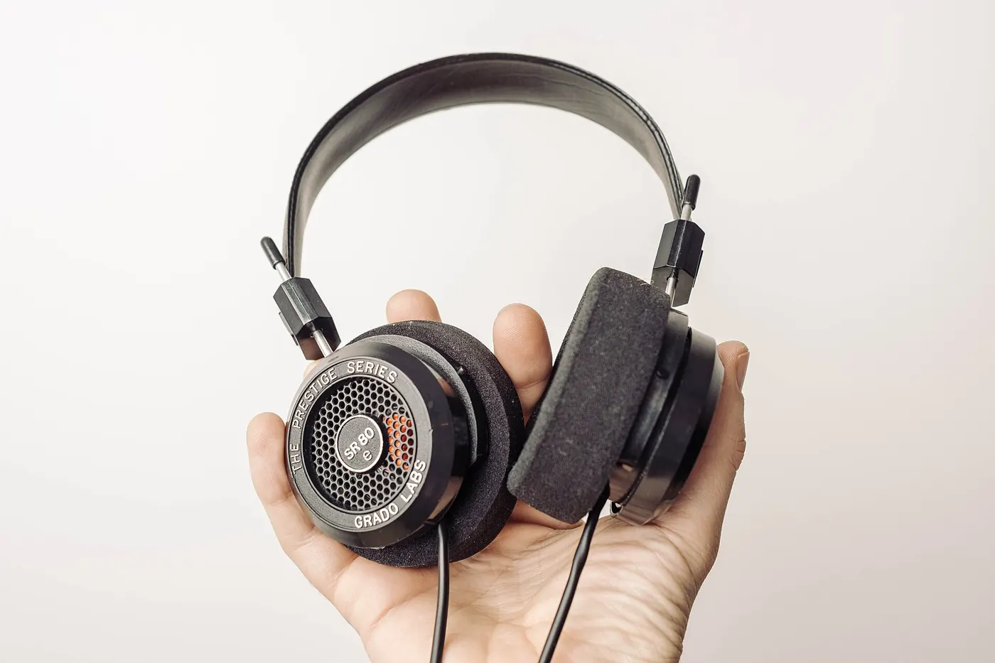 A hand holding a pair of on-ear headphones against a pale background